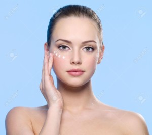 8928575-Portrait-Of-Young-Adult-Girl-Applying-Cream-On-Her-Skin-Around-Eyes-Blue-Background-Stock-Photo